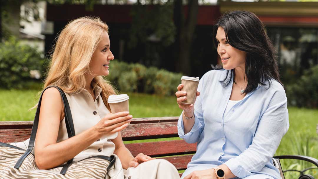 two mature women chatting with coffee in park